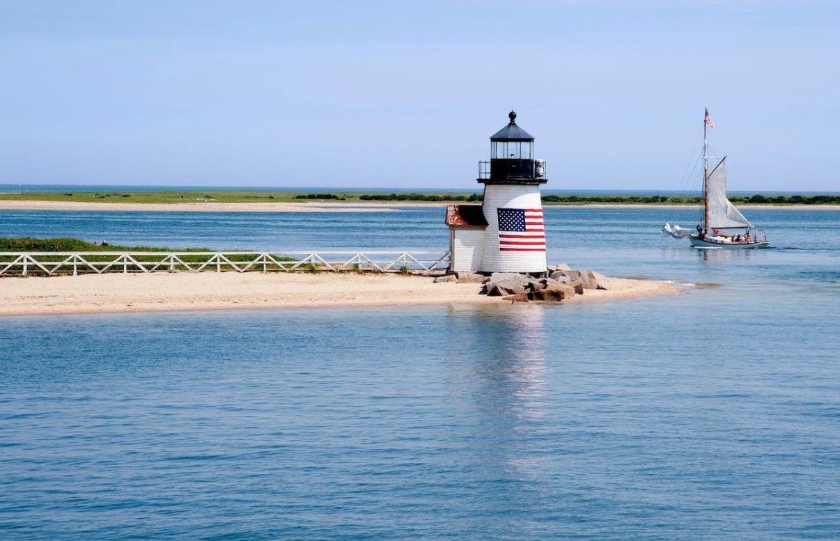 Brant Point Light with the American flag on its tower, a sailboat passing behind.