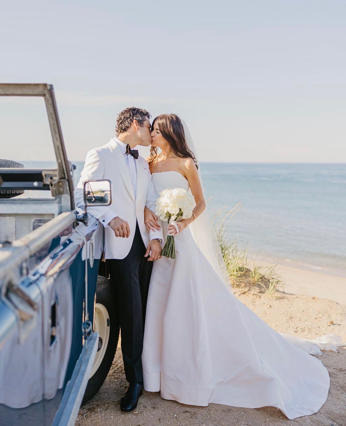 A bride and groom beside the open door of the Land Rover on the beach.