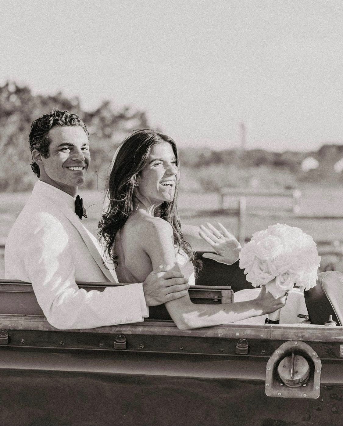 The couple riding in the back of the open Land Rover, in black and white.