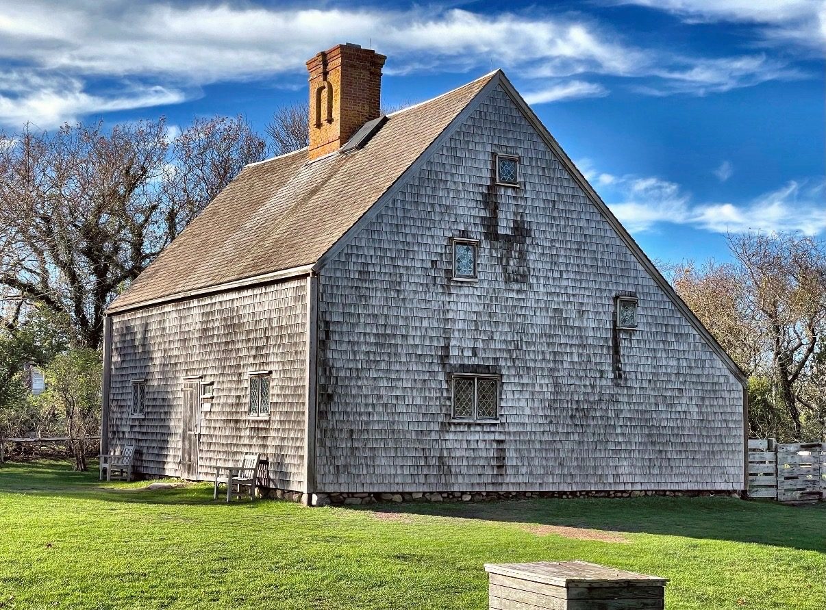 The Oldest House, a weathered shingled saltbox on a lawn under a blue sky.